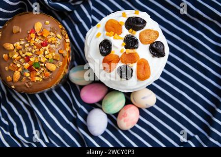 Delicious Easter cakes with colorful eggs on striped fabric. Two cakes, one with white frosting, the other with chocolate frosting and mixed nuts. Mul Stock Photo