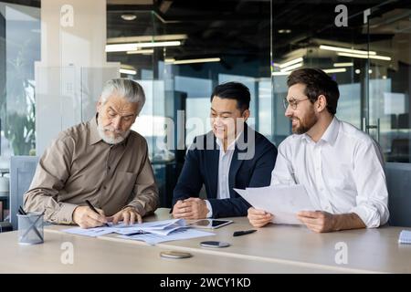 Three businessmen collaborating on financial documents in a bright office environment, depicting teamwork, strategy, and professionalism. Stock Photo