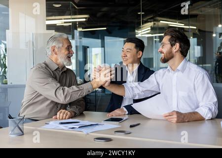 Three smiling male professionals celebrate a successful partnership in a bright, contemporary office setting, highlighting teamwork and achievement. Stock Photo