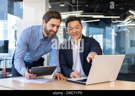 Two professional businessmen working together at a modern office space. Discussing strategy with a laptop and documents. Stock Photo