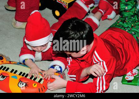 Sibling brothers one decked out in a Santa Claus suit, play with an opened present on Christmas morning. Stock Photo