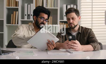 Two businessmen multiracial men co-workers in office Arabian Indian businessman show papers business project on laptop to colleague Caucasian man Stock Photo