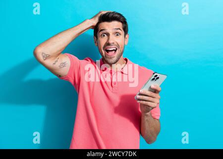 Portrait of young confused guy using smartphone betting all his money in online casino he lost isolated on aquamarine color background Stock Photo