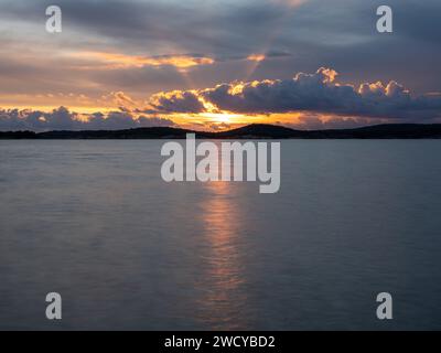 Clouds and atmosphere in warm evening colors with the sun behind the cloudsl Light reflecting in the sea. Stock Photo