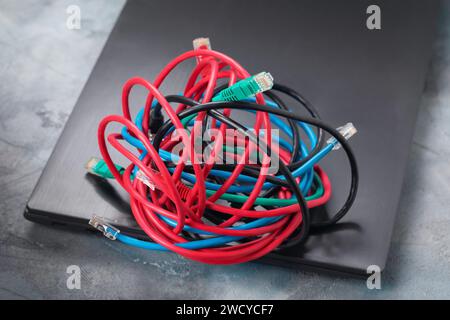 A pile of network wires on a laptop, a concept on the topic of confusion in connecting to a local network or the Internet via wire and the transition Stock Photo