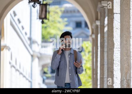 Dark-haired man walking through the arch and talking on the phone Stock Photo