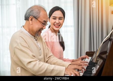 Happy daughter and elderly father playing music on the piano together in living room Stock Photo