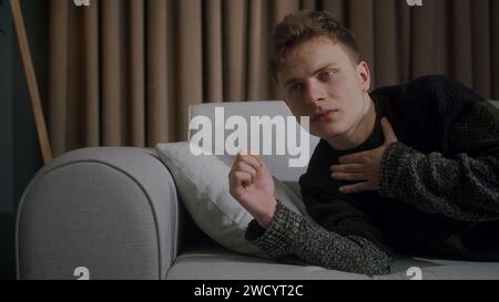 Side shot of young man suddenly wakes up while sleeping on sofa at home due to anxiety, disorder, bad dreams and illness or disease Stock Photo