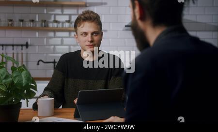 Two co-worker men are sitting in the kitchen having a fun chat. Taking a break at work, technology company workers, relaxing time Stock Photo