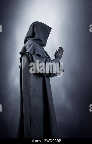 Medieval monk in hooded cloak praying in the dark Stock Photo