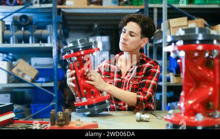 Female worker assembles shutoff valves using various tools in factory indoor Stock Photo