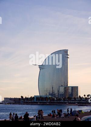 Barcelona, Spain - November 20, 2022: W Barcelona hotel with an airplane approacing. Barceloneta beach in the front is full of people.  Stock Photo