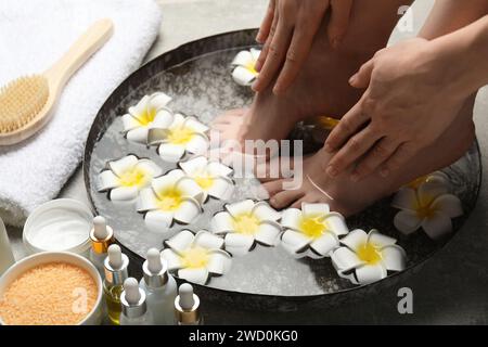 Woman soaking her feet in bowl with water and flowers on floor, closeup. Spa treatment Stock Photo