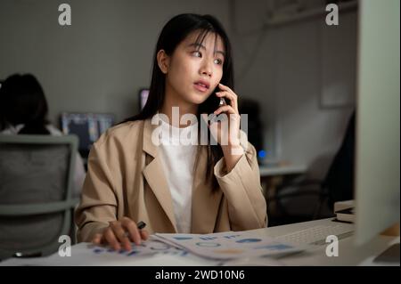 A professional Asian businessman is talking on the phone with her supplier, having a serious phone call, working at her desk in the office. Stock Photo