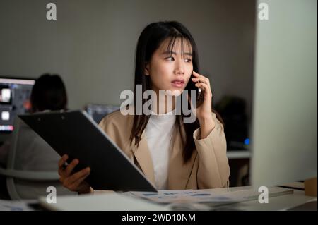 A professional Asian businessman is talking on the phone with her supplier, having a serious phone call, working at her desk in the office. Stock Photo