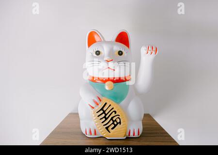 White Chinese Lucky Cat waving statue on the wooden shelf on the white background Stock Photo