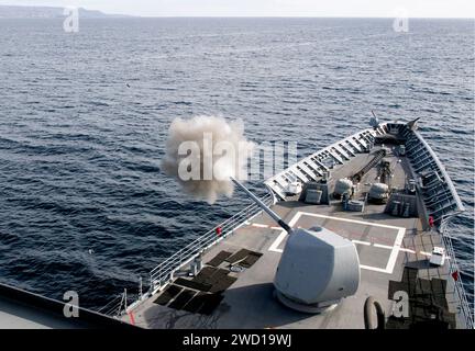 A Mark 45 5-inch gun fires off the port side of guided-missile cruiser USS Lake Champlain. Stock Photo
