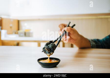 Black Fried Gyoza is taken using black chopsticks by a hand with bokeh background Stock Photo