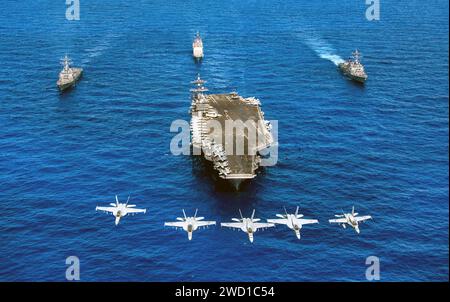 F/A-18 Hornets fly over a formation of U.S. Navy ships transiting the Pacific Ocean. Stock Photo