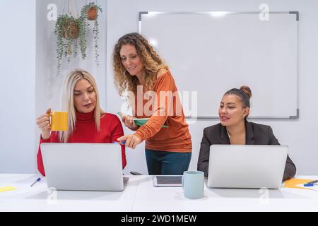 Three professionals engage in a productive meeting, laptops open, discussing over notes and coffee.  Stock Photo