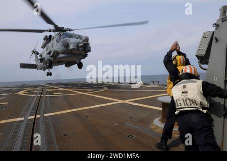 Boatswain's Mate signals to an MH-60R Sea Hawk on the flight deck of USS Wayne E. Meyer. Stock Photo