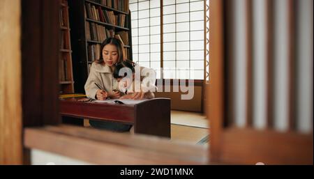 Mother, child and drawing helping or pencil for home schooling lesson, Japanese or tutor. Female person, girl daughter and book paper in Tokyo or Stock Photo