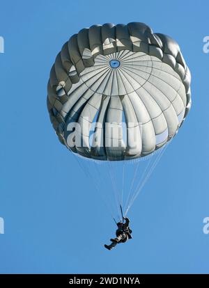 An explosive ordnance disposal technician descends under a parachute during static line free-fall training. Stock Photo