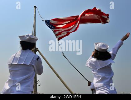 Sailors raise the ensign as the aircraft carrier USS Nimitz shifts colors after mooring in Bahrain. Stock Photo