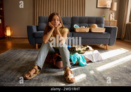 Young overwhelmed woman having trouble packing suitcase for vacation trip Stock Photo