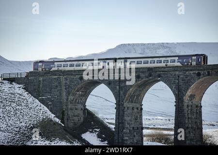 A Northern train crossing the railway on the Ribblehead Viaduct in the snow in the Yorkshire Dales National Park. Taken on a beautiful blue sky day. Stock Photo