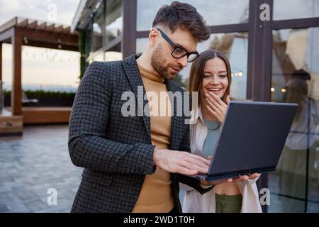 Man and woman using laptop standing together on roof terrace Stock Photo