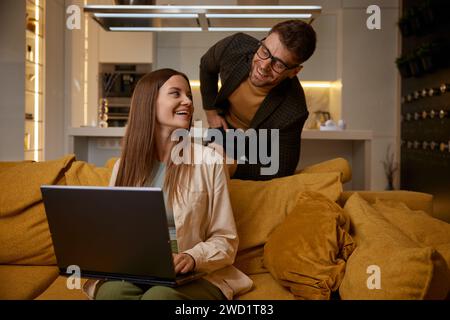 Happy stylish couple resting at home watching funny video on laptop Stock Photo