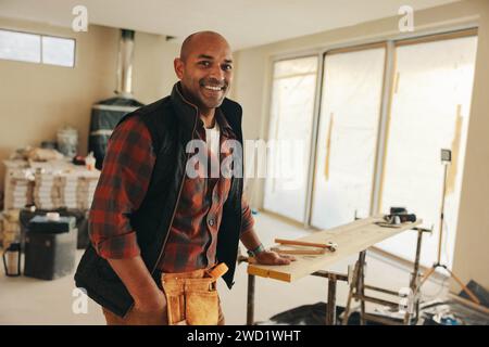 Mature man with a tool belt stands happily in his home kitchen, looking at the camera confidently. Homeowner using his expertise in home improvement i Stock Photo