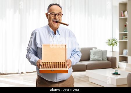 Mature man smoking a cigar at home and holding a box of cigars Stock Photo