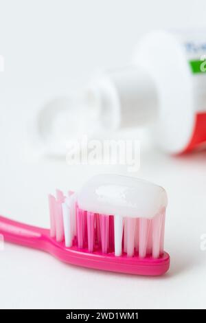 Close up of a single plastic toothbrush head with a strip of white toothpaste on it and a tube of toothpaste in the background Stock Photo