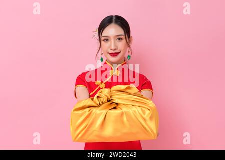 Chinese new year portrait of elegant Asian woman in traditional cheongsam dress giving golden gift box in pink color background Stock Photo