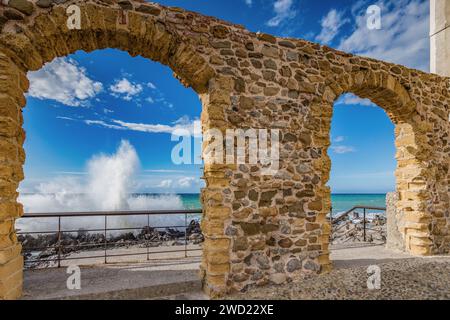 Waves crashing on the rocks seen from a stone arch in Cefalù pier, Sicily Stock Photo