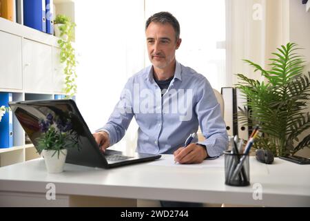 Businessman in blue shirt working with a laptop typing and taking notes in the office. Stock Photo