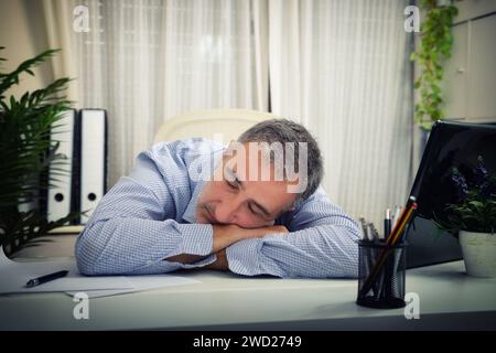 Detail of a man sleeping on an office table with a laptop and pen in an office. Stock Photo