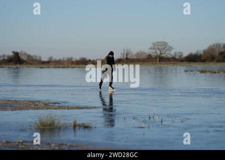 Fen skaters on a frozen flooded field in Upware, Cambridgeshire. The UK will remain in a cold snap until the weekend with freezing temperatures set to plummet even further across much of the country. Picture date: Thursday January 18, 2024. Stock Photo