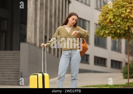 Being late. Worried woman with suitcase and backpack looking at watch outdoors Stock Photo