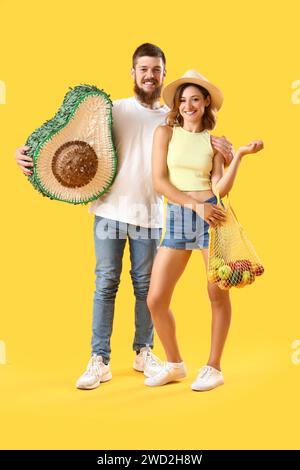 Happy couple in love with Mexican pinata and string bag on yellow background Stock Photo