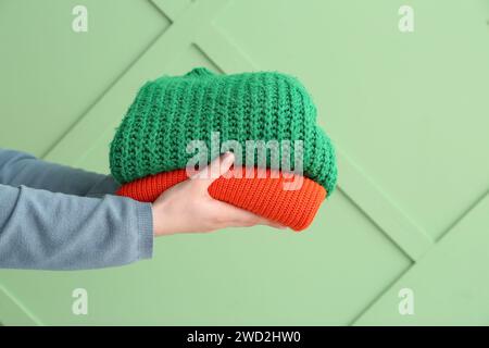 Female hands with stack of different stylish sweaters on green background Stock Photo