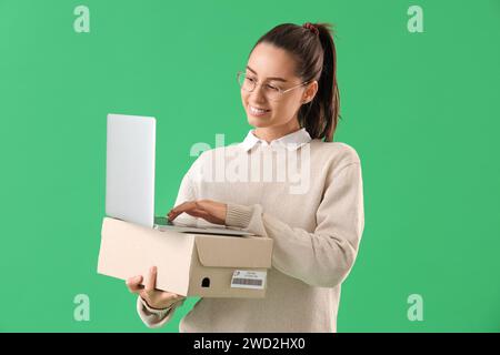 Female seller with parcel using laptop on green background Stock Photo