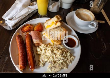 12 December 2023: Breakfast with fried sausages, toast and scrambled eggs on a plate on a set table with cappuccino and orange juice *** Frühstück mit gebratenen Würsten, Toast und Rührei auf einem Teller auf einem gedeckten Tisch mit Cappuccino und Orangensaft Stock Photo