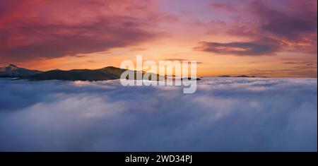 Beautiful sunrise high in the mountains above the clouds. Dramatic natural landscape with mountains, fog and sky. Stock Photo