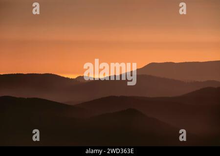 Beautiful landscape with silhouettes of mountain ranges at sunrise with orange sky. Stock Photo