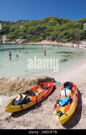 Cala Galdana, Menorca, Balearic Islands, Spain. Tourists enjoying the clear turquoise waters of Cala Macarella, beached kayaks in foreground. Stock Photo