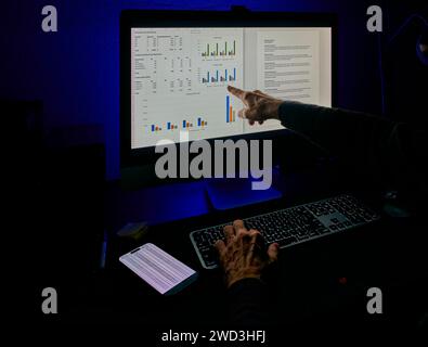 A professional points at financial graphs on a monitor, analyzing and discussing data. Stock Photo