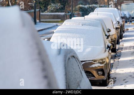 Line of vehicles covered in a layer of snow parked on the street on a ...